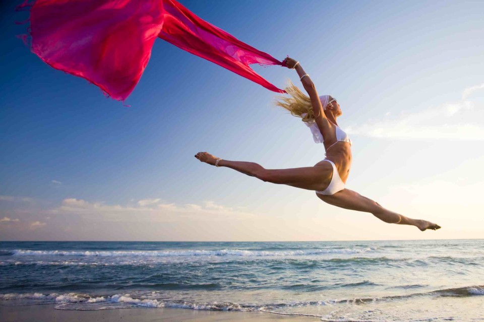 Young woman with scarf jumping on beach