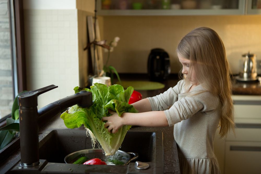 Little girl washes vegetables