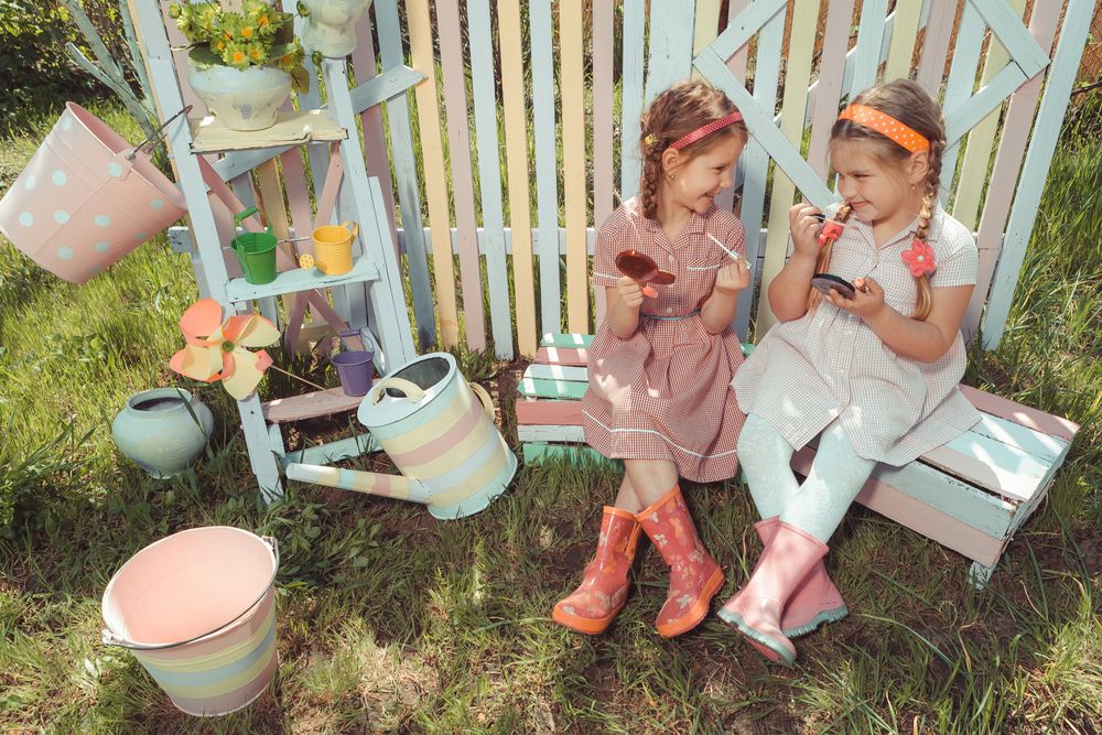 Little girls with lipstick and holding mirror in garden