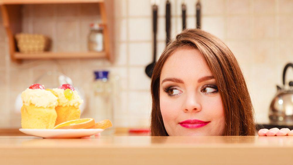 woman-hidden-behind-table-sneaking-and-looking-at-delicious-cake-with-sweet-cream-and-fruits-on-top