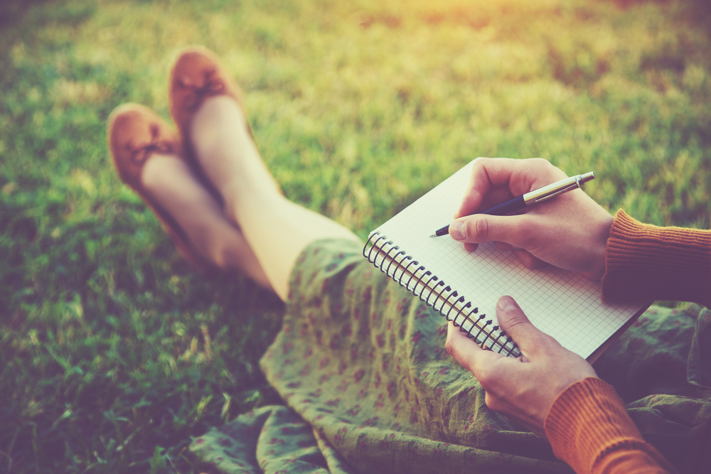 Green journalist woman with notebook and pen on grass